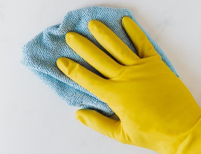 Yellow gloved hand holding blue microfiber cloth on white surface